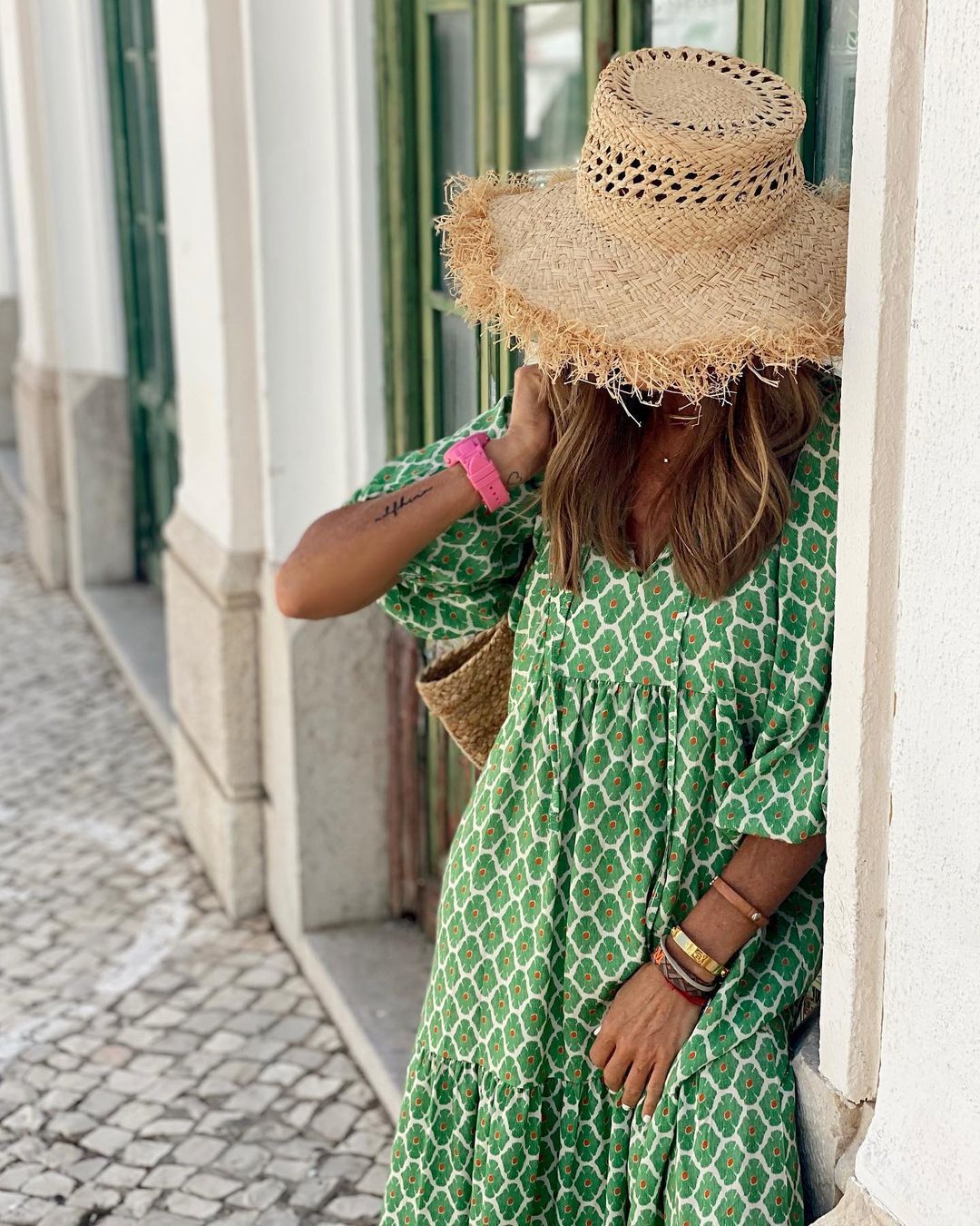 A woman in a summer bohemian v-neck dress stands by green doors, showcasing a flowy silhouette and boho-inspired design.