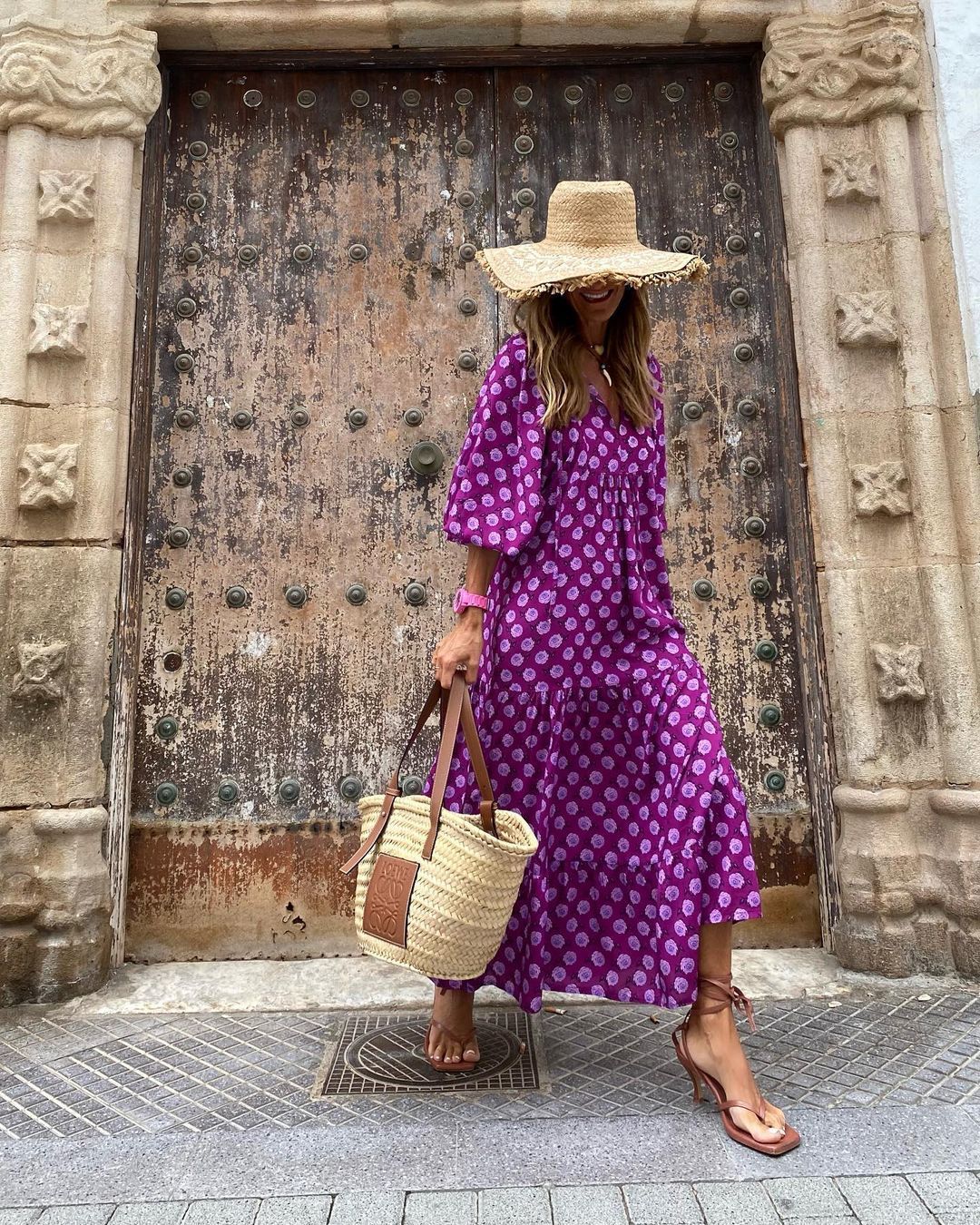 Model wearing a summer bohemian v-neck dress in purple print, accessorized with a wide-brimmed hat and straw bag.