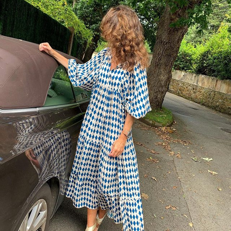 A woman in a summer bohemian v-neck dress stands by green doors, showcasing a flowy silhouette and boho-inspired design.
